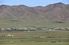 Cluster of tents and grazing herds on open plateau below brown hills.