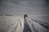Single car on a snowy ice road with deep tracks and a church in the distance