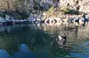 Scuba diver on calm water near a rocky, tree-lined shore