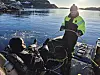 A man in scuba gear and another in high-vis gear on a small boat in a calm icy inlet