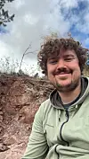 Man in a hoodie smiling on a rocky hillside under a cloudy sky