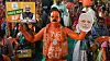 BJP supporter with orange body paint holding a party sign and face cut-out in a rally crowd