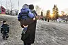 Adult carries a child in winter clothes across a frosty kindergarten playground at sunrise.