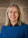 Smiling woman in blue jumper standing before a stone wall