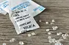 Silica gel desiccant packets with clear beads scattered on a wooden surface.