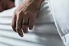 Man's hand with ring hanging over the side of a white bed