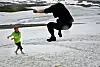 Two people playing on a snowy slope in Norway, one mid-air in a jump.