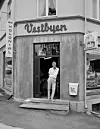 Black and white street view of Vestbyen Kolonial with a man standing in the doorway.