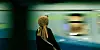 Person in a headscarf standing on a station platform as a train rushes past.