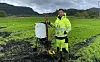 Dr Junbin Zhao in high-visibility gear beside field soil equipment on wet farmland.