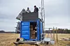 Two researchers install instruments on a blue container at a rural Pasvik field site in Norway.