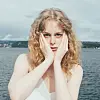 Woman with curly blond hair holding her face while standing by the water