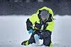 Researcher in bright jacket kneels on snowy ice, filling a sample bottle.