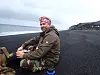 Field researcher sitting on a black sand beach at Deception Island in cloudy weather.