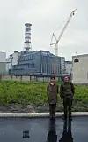 Two people stand near a nuclear reactor building with a crane in the background.