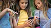 Three children sit together and look at a smartphone outdoors.