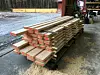 Stacked spruce boards in a lumber yard beside a gravel surface and workshop area.