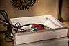 Coin cell and circuit board with test leads inside an air bath test chamber.