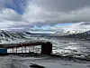 Rusted pipeline above a snowy valley with distant mountains under cloudy skies