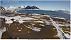 Snow-dotted Arctic tundra leading to a bay with snow-covered mountains under a clear sky