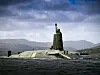 HMS Vigilant Vanguard-class Royal Navy submarine on the surface with hills in the background.