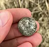 Hand holding an old silver coin in a grassy field.