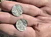 Dusty hand holding two small silver coins with engraved heads and lettering.