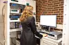 Researcher standing at a computer next to racks of electronic equipment in a lab.