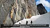 People walk at the base of a steep mountain cliff with visible magma dikes in Sarek National Park.