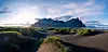 Mountain above black sand dunes beneath a cloudy sky.