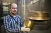 Museum visitor holding a brass vessel in a display gallery.