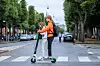 Two people ride a Lime electric scooter across a crosswalk on a city street in Copenhagen.