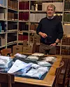 Professor Svein Harald Gullbekk stands in front of a table with many bags containing coins from the Mørstad hoard, surrounded by bookshelves full of books.