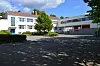 Holtet Public High School in Oslo with white buildings, trees and a paved courtyard under a blue sky.