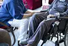 Health worker seated beside a patient in a wheelchair during a conversation.
