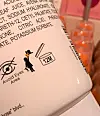 Close-up of a cosmetic bottle label with ingredient text, warning icons and a 12M symbol.