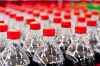 Rows of clear plastic bottles with red caps in a factory-like setting.