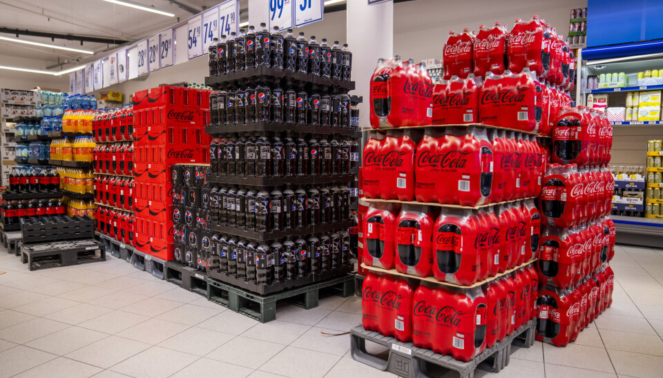 Pallet stacks of Pepsi Max and Coca-Cola Zero Sugar bottles in a Rema 1000 supermarket aisle.