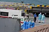Health workers in protective gear escort patients from a cruise ship onto a port walkway.