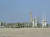 Industrial plant with tall towers and piping in a dry, sandy landscape.