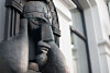 Close-up of a dark statue wearing a helmet beside a blurred building facade.