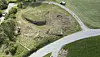 Aerial view of a curved road beside a fenced grassy field with bare patches.