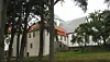 Historic stone buildings partly hidden by tall trees on a grassy slope.