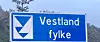 Blue road sign reading Vestland fylke beside a mountain landscape.