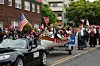 Parade with people in traditional clothes, American and Norwegian flags, as well as a decorated boat on a trailer.