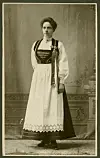 Sepia-toned full-length portrait of a woman in a traditional dress standing in a studio.