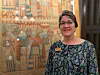 Woman standing beside a large mural in a museum exhibition space.