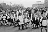 Children in traditional Norwegian dress march with flags in a Brooklyn parade as spectators watch.