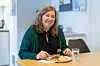 Woman sits at a table with a plated meal and a glass of water in an office setting.