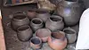 Assorted handmade clay pots and vessels arranged on the ground in a pottery workspace.